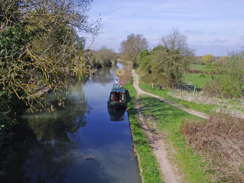 The Basingstoke Canal near Odiham, with a narrowboat moored by the towpath under a blue sky
