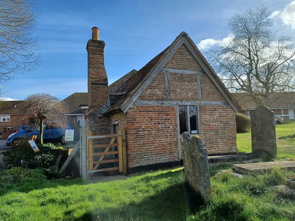 Odiham's Pest House, a small 17th-century brick cottage with a tiled roof in the corner of the churchyard
